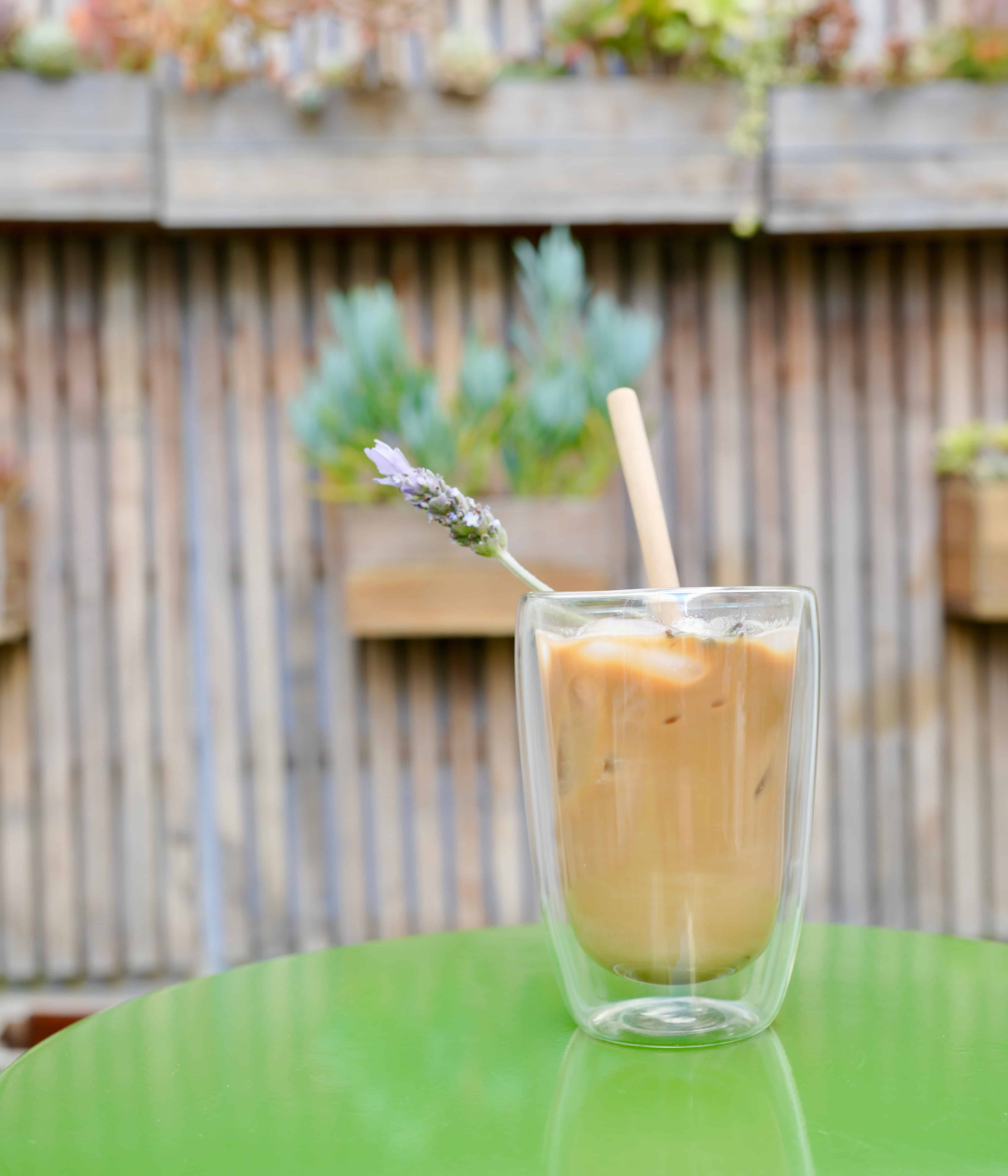 Ice Latte with straw on green patio table in front of succulent vertical garden wall
