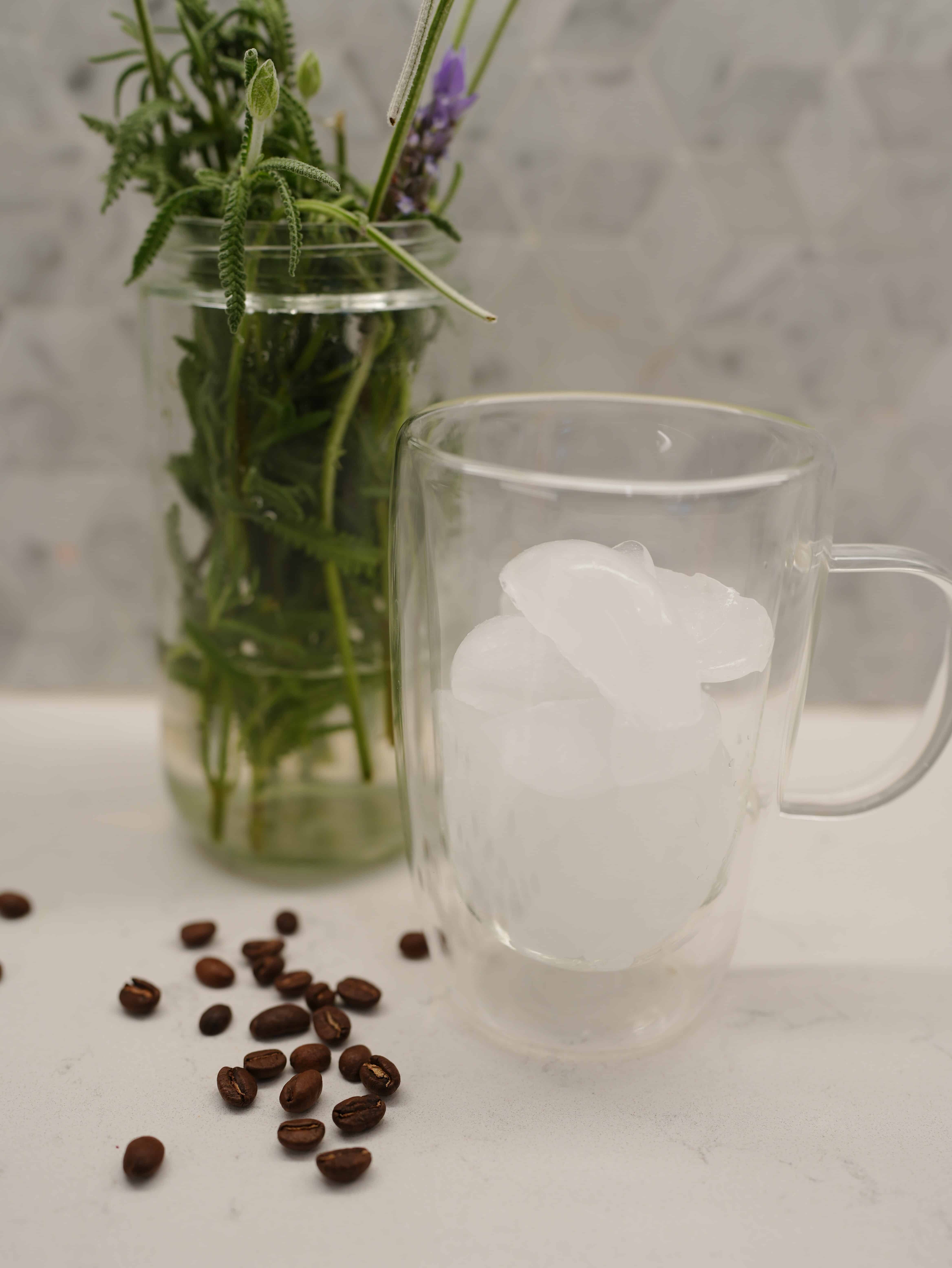 Ice filled glass jar sitting next too coffee grounds and lavender plant in glass jar