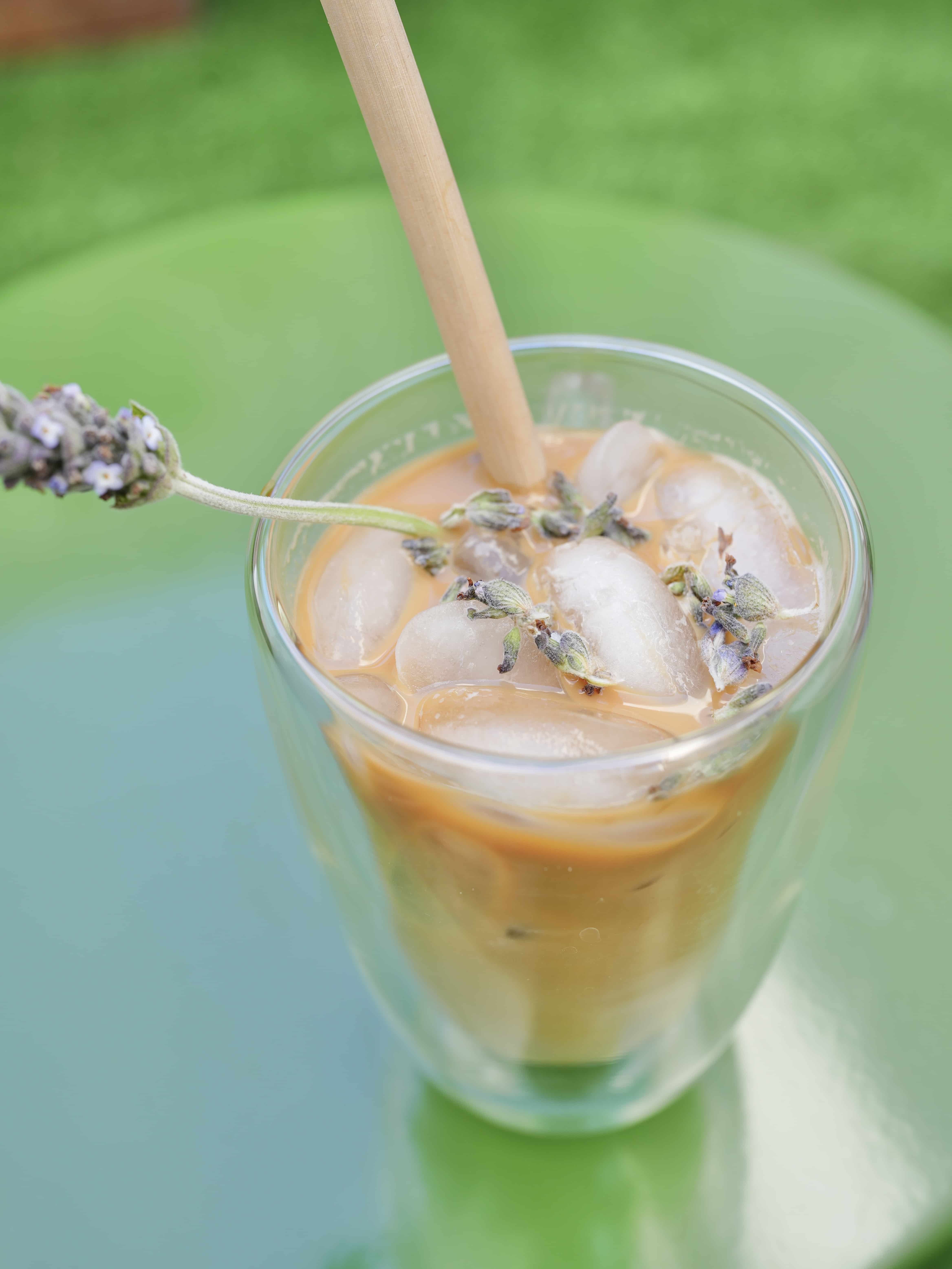 Lavender Iced Latte in glass jar with wooden straw on green background