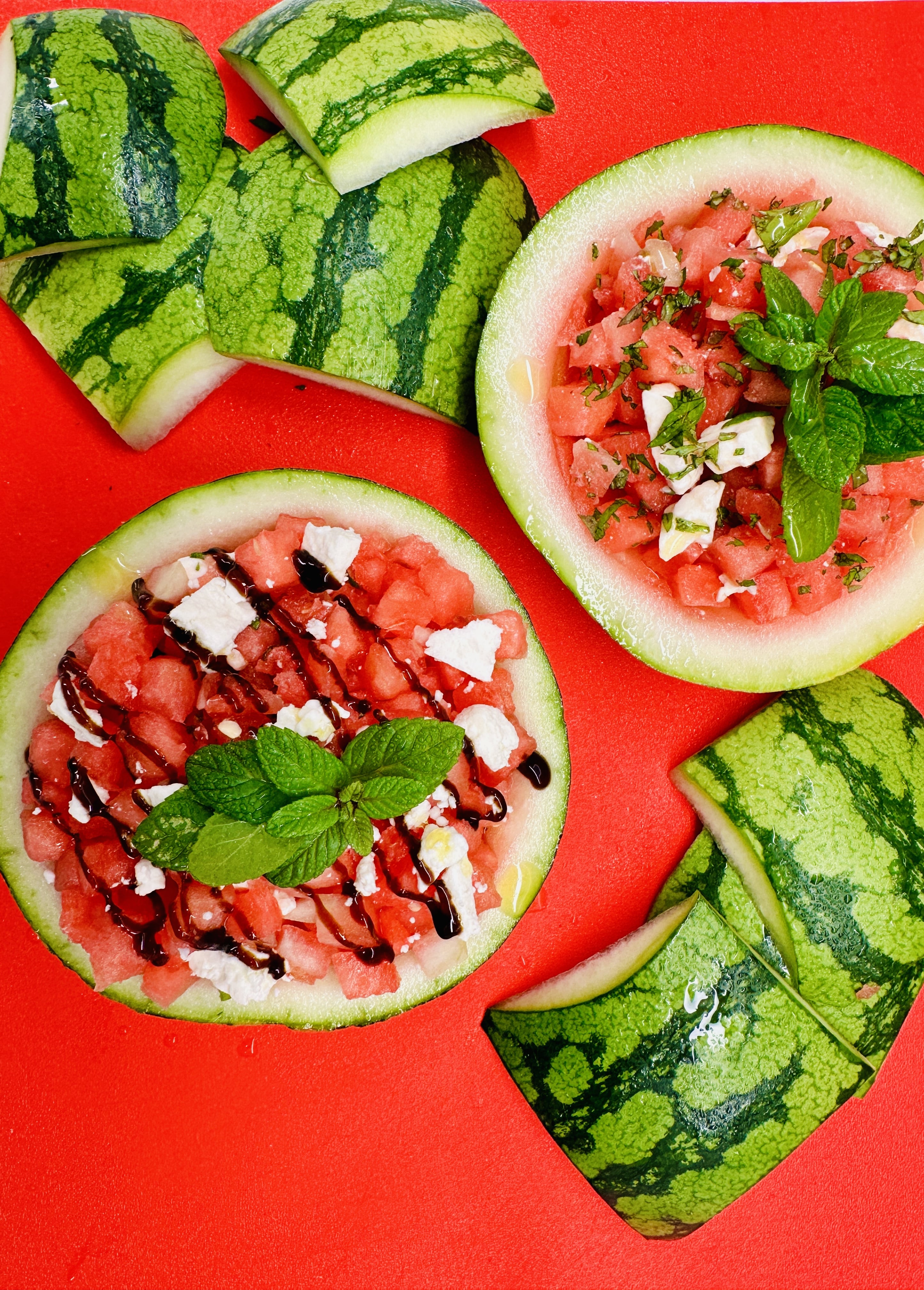Watermelon salad inside watermelon husks on red cutting board