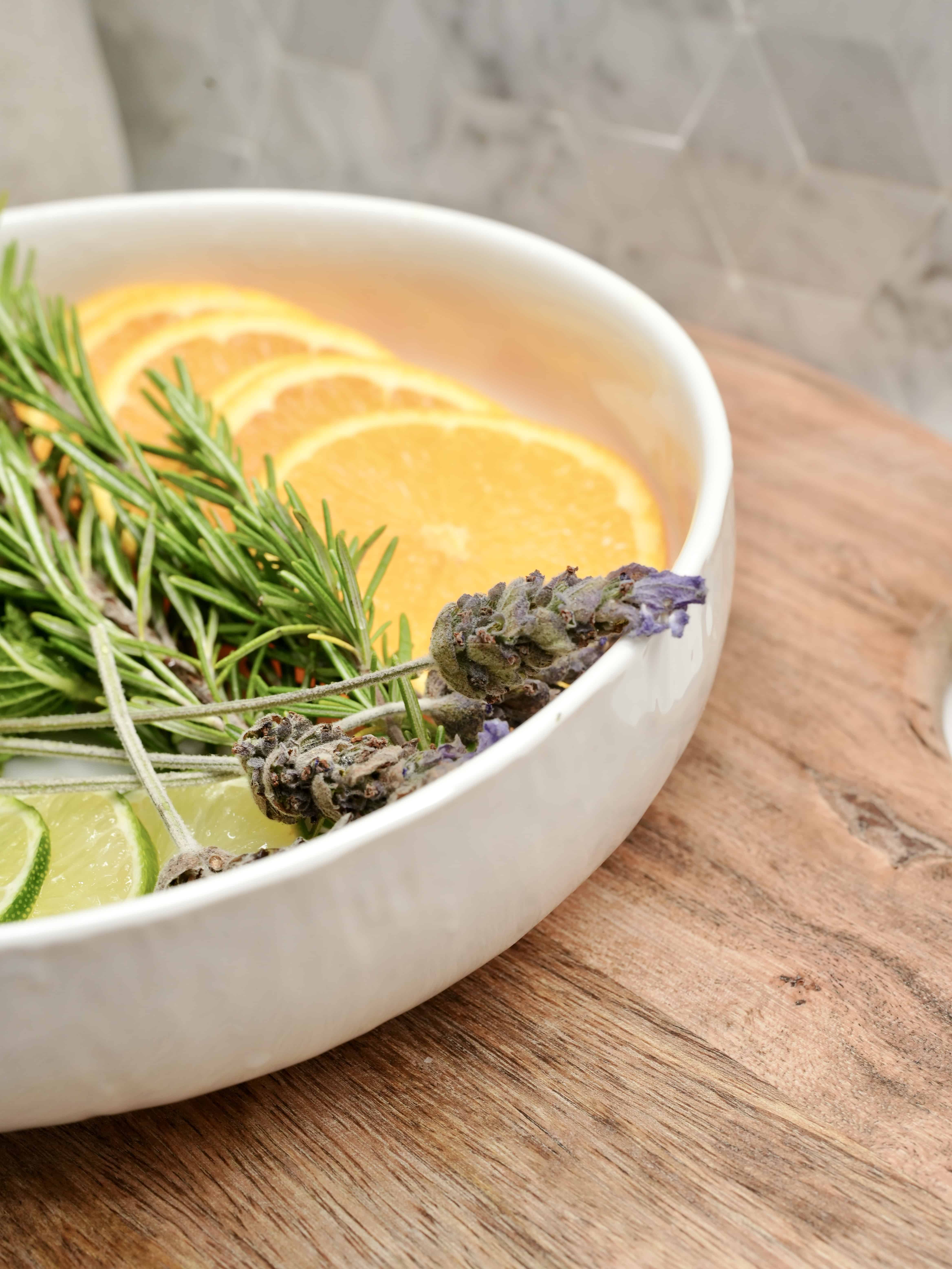 Lavender flowers, citrus, and rosemary in white bowl on cutting board