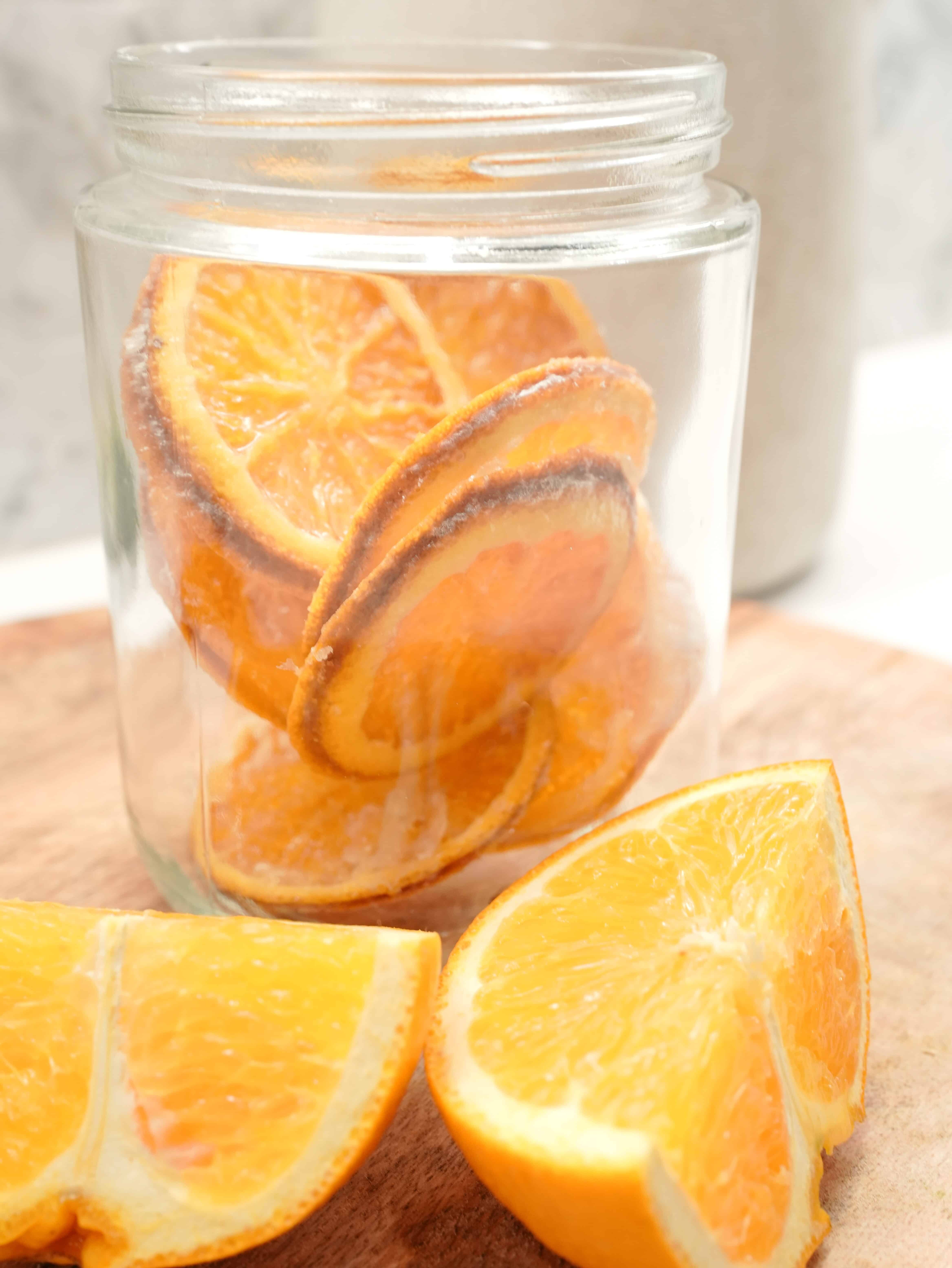 Candied Dehydrated Sliced Oranges inside Glass jar next to freshly sliced oranges on cutting board